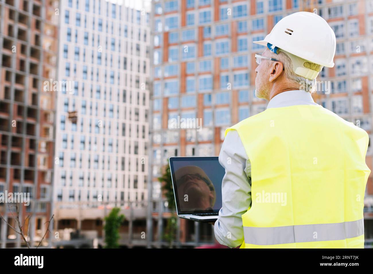 Rückansicht alter Mann mit Helm, der Laptop hält Stockfoto