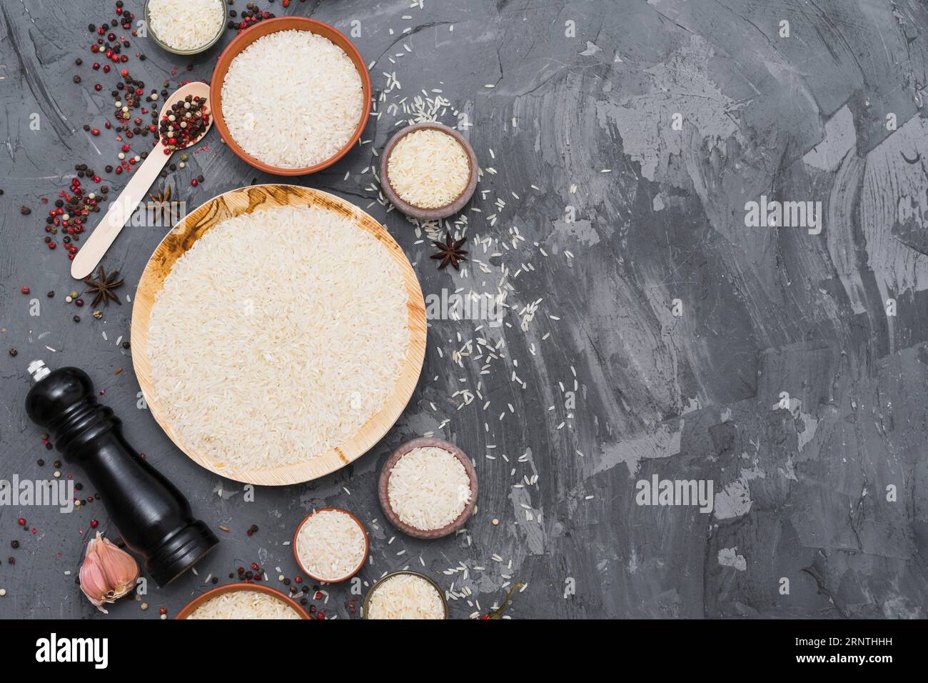 Weißer roher Reis mit trockenen Gewürzen Knoblauchzehe Pfeffermühle Betonkulisse Stockfoto