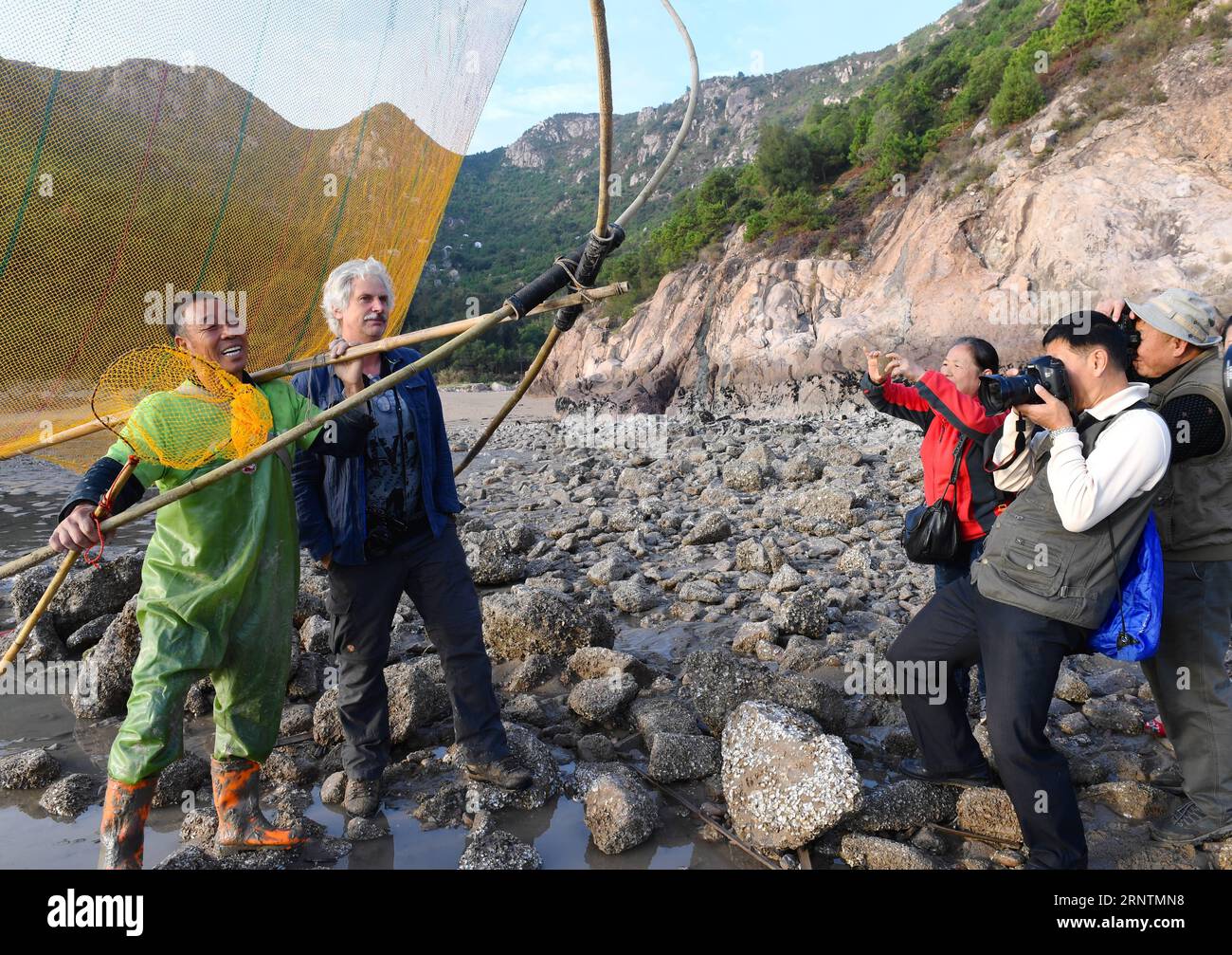 (171113) -- XIAPU, 13. November 2017 -- Jiang Lianshui (1. L) posiert für Fotografen im Beiqi Village im Xiapu County, Provinz Fujian im Südosten Chinas, 9. November 2017. Xiapu County mit 480 km Küste und 69.333 ha Schlammfläche ist berühmt für seine malerische Landschaft mit Stränden und zieht Gruppen von Fotografen an, um Fotos zu machen. So steigt die Nachfrage nach Modellen, die den Fang auf traditionelle Weise darstellen können. Der 67-jährige Jiang Lianshui ist eines dieser neuen Modelle. Jiang wechselte seine Karriere von einem Fischer zu einem Vollzeitmodell im Jahr 2007. Er ist zufrieden Stockfoto
