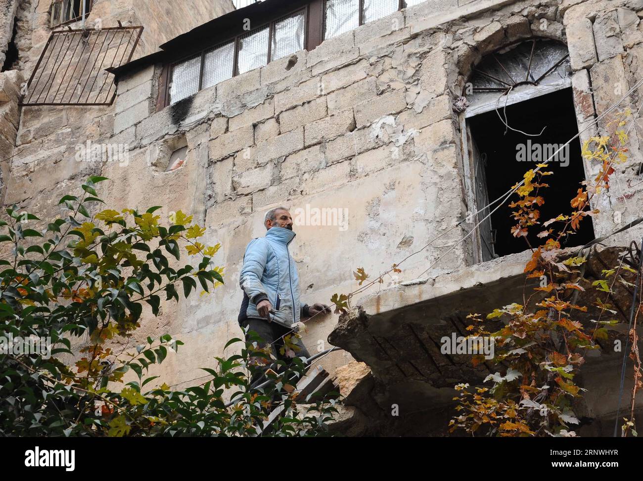 (171221) -- ALEPPO, 21. Dezember 2017 -- Maher Khayata, ein 60-jähriger Mann, klettert am 21. Dezember 2017 eine prekäre Leiter über die zerstörte Treppe zu seinem Haus auf dem Dach eines zerbrochenen Einkaufszentrums in der Altstadt von Aleppo, Nordsyrien. Khayata ist der Hüter eines Einkaufszentrums. Er hat sein Leben damit verbracht, das Gelände zu schützen und dafür zu sorgen, dass es sicher bleibt. Als der Krieg sein Leben erschütterte und alles in Trümmer zerquetschte, blieb er dort und bewachte jede Erinnerung an ihn mit jedem fallenden Felsen in der Altstadt. Auf dem Foto steht der artikel Feature: Syrischer alter Mann wacht im Krieg Stockfoto