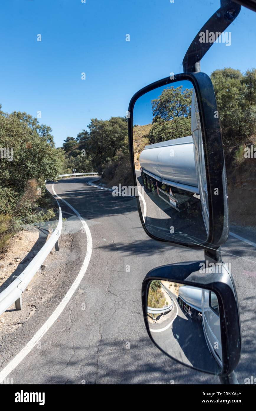 Rückspiegel eines Lkws, wo Sie die scharfe Kurve auf der gesamten Straße des Tankwagens auf einer schmalen Bergstraße sehen können. Stockfoto