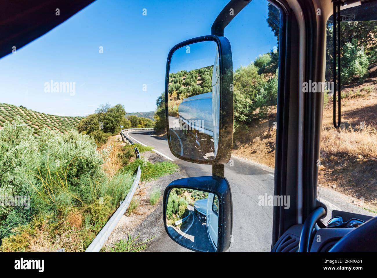 Rückspiegel eines Tanklastwagens, der auf einer schmalen Bergstraße fährt und in Kurven die gesamte Straße einnimmt. Stockfoto
