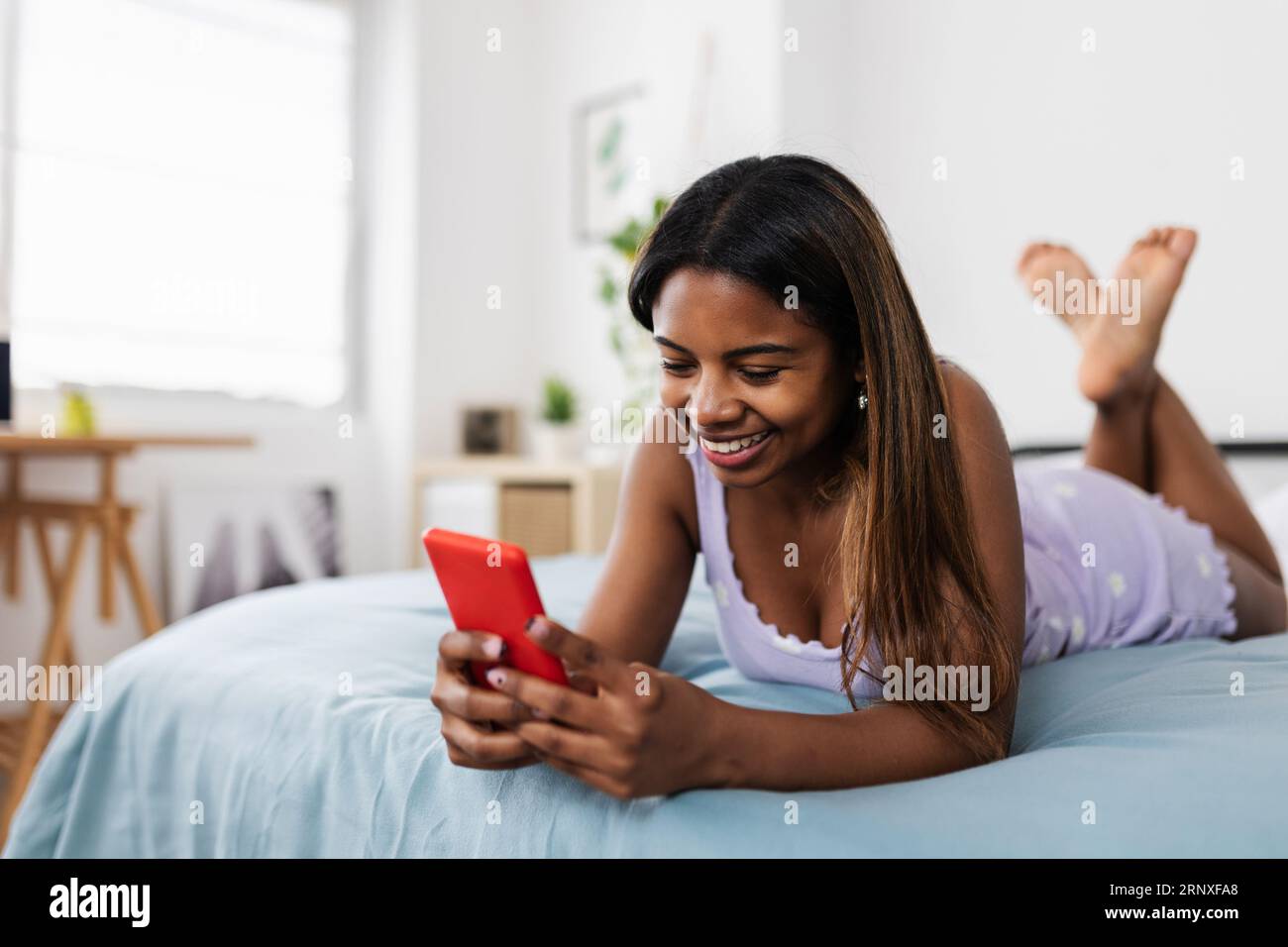 Junge lateinische Schülerin mit Smartphone, während sie sich zu Hause im Bett entspannt Stockfoto