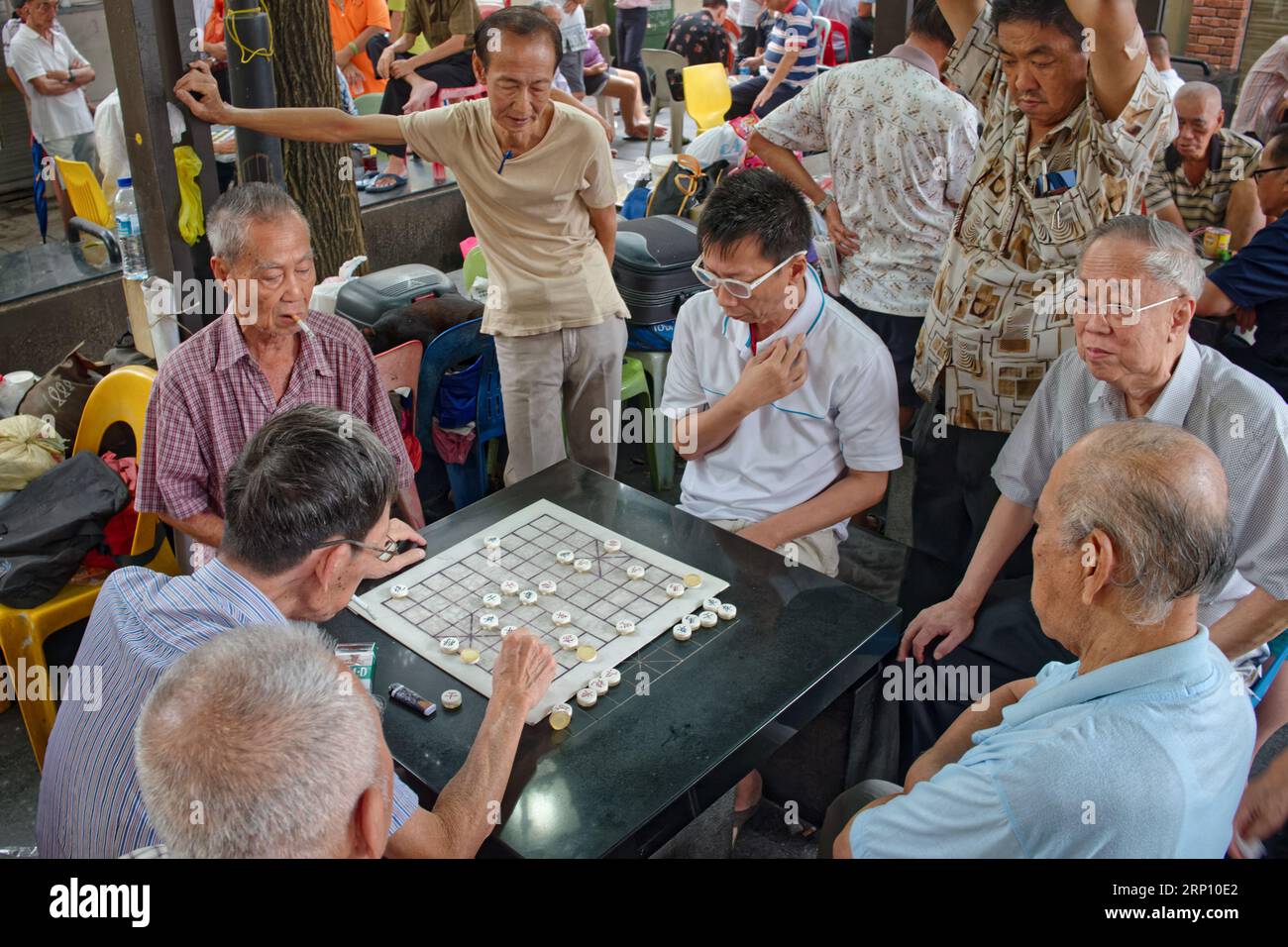 Ältere, pensionierte, ethnische Chinesen auf dem Kreta Ayer Square, Chinatown, Singapur, spielen eine chinesische Schachvariante, beobachtet von neugierigen Zuschauern Stockfoto