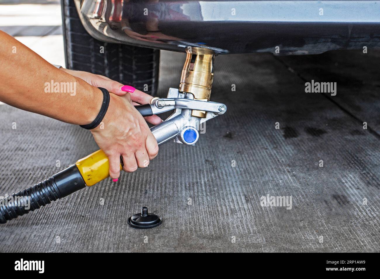 Weibliche Mitarbeiter mit gut gepflegten Händen, die die Gaspistole nach dem Tanken des Autos für einen LPG-Kunden entfernen, mit einer Verbindung zur Wirtschaft und der Welt Stockfoto