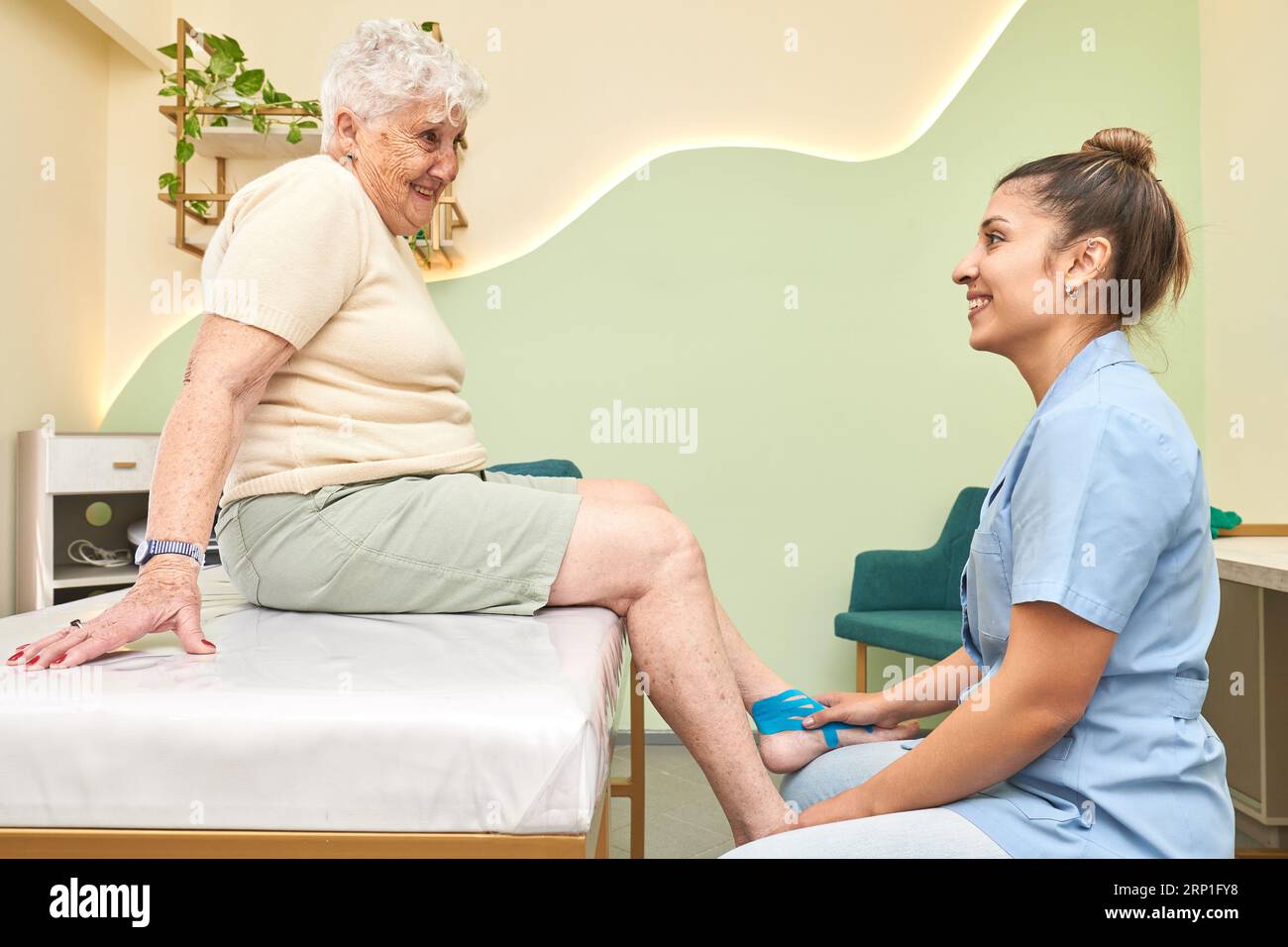 Arzt und älterer Patient sprechen während des Aufbringens des blauen kinesio-Klebebandes Stockfoto