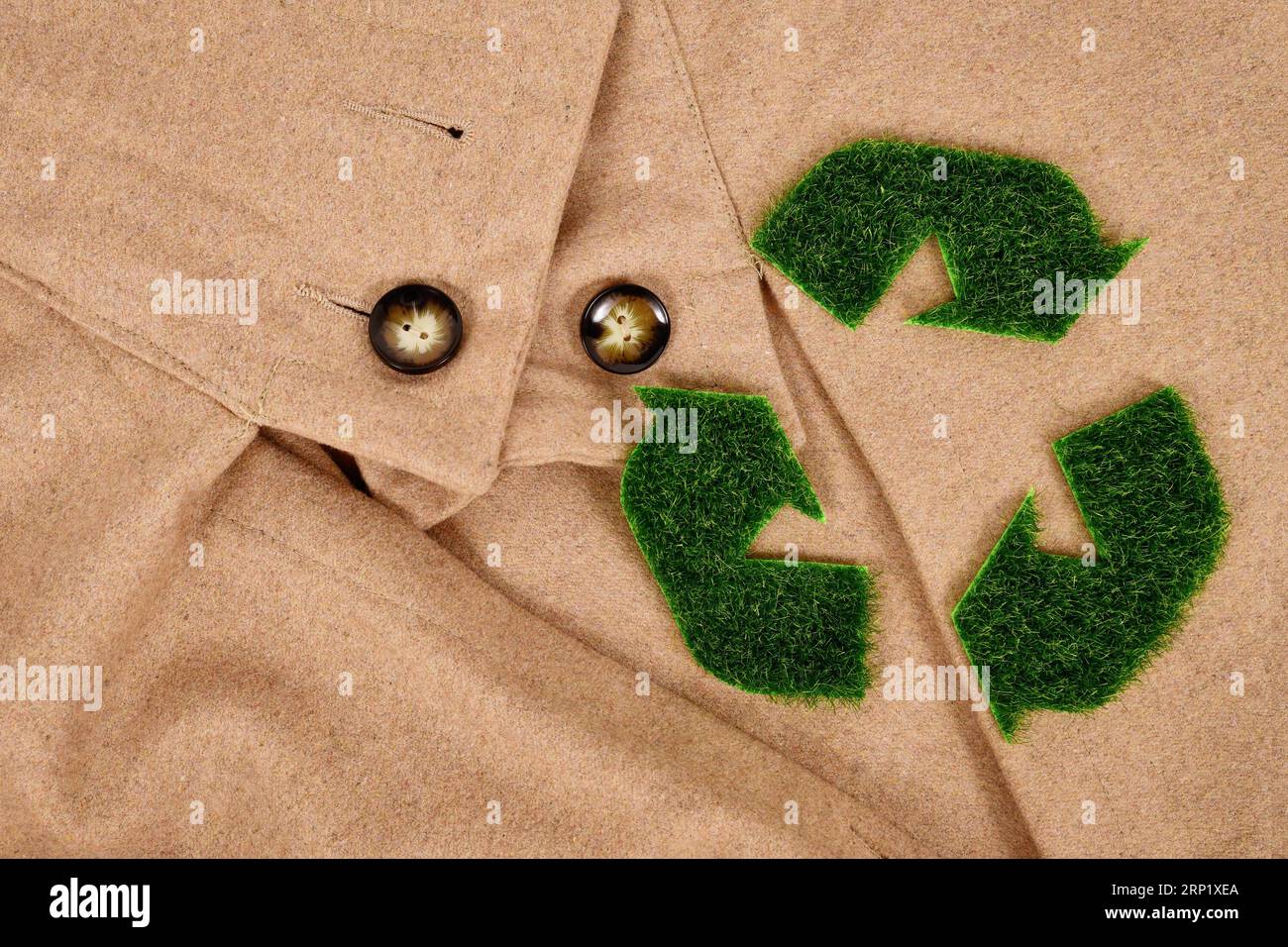 Recycling-Pfeilsymbol aus Gras auf beigefarbenem Mantel. Konzept für umweltfreundlich produzierte Kleidung Stockfoto