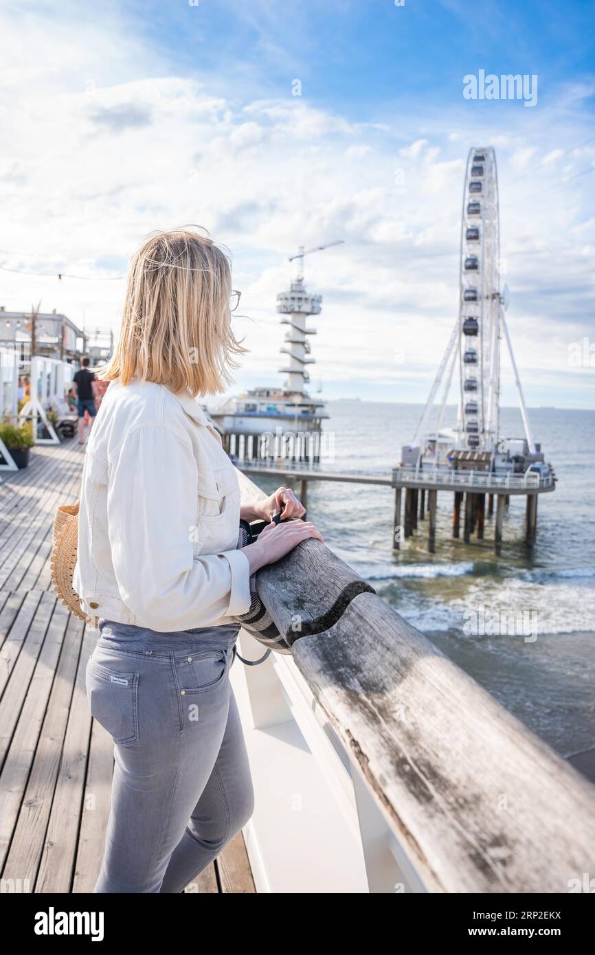 Touristen, die auf dem Pier stehen und auf das Riesenrad blicken, den Haag, Niederlande Stockfoto