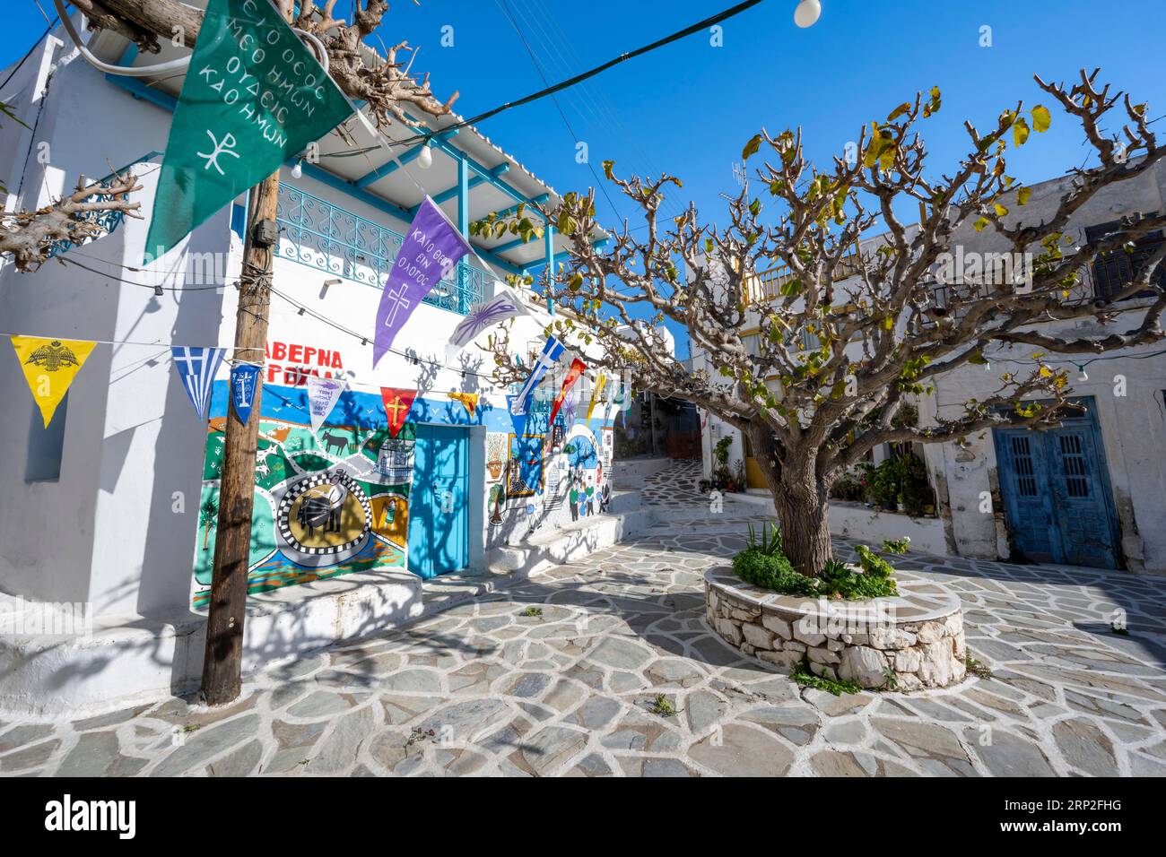 Kleiner Platz mit bemalten Häusern, Bäumen und bunten Fahnen, Gassen des Dorfes Marpissa, Paros, Kykladen, Griechenland Stockfoto