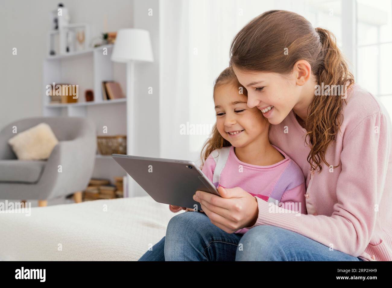 Zwei lächelnde Schwestern, die mit dem Tablet zu Hause sind Stockfoto