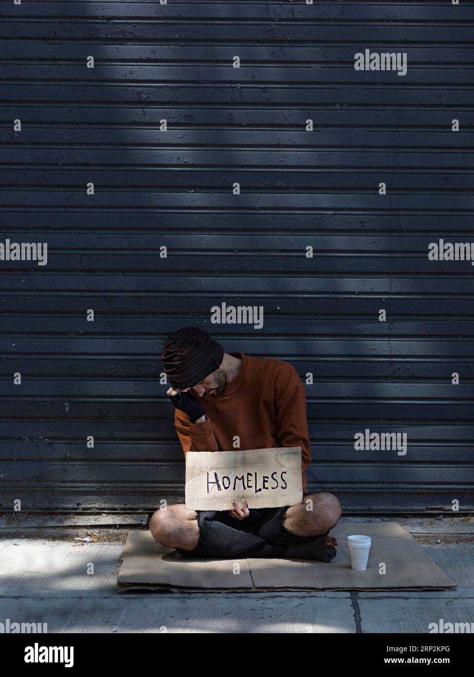 Obdachloser Mann, der sein Gesicht versteckt und Geld nach langer Sicht fragt Stockfoto
