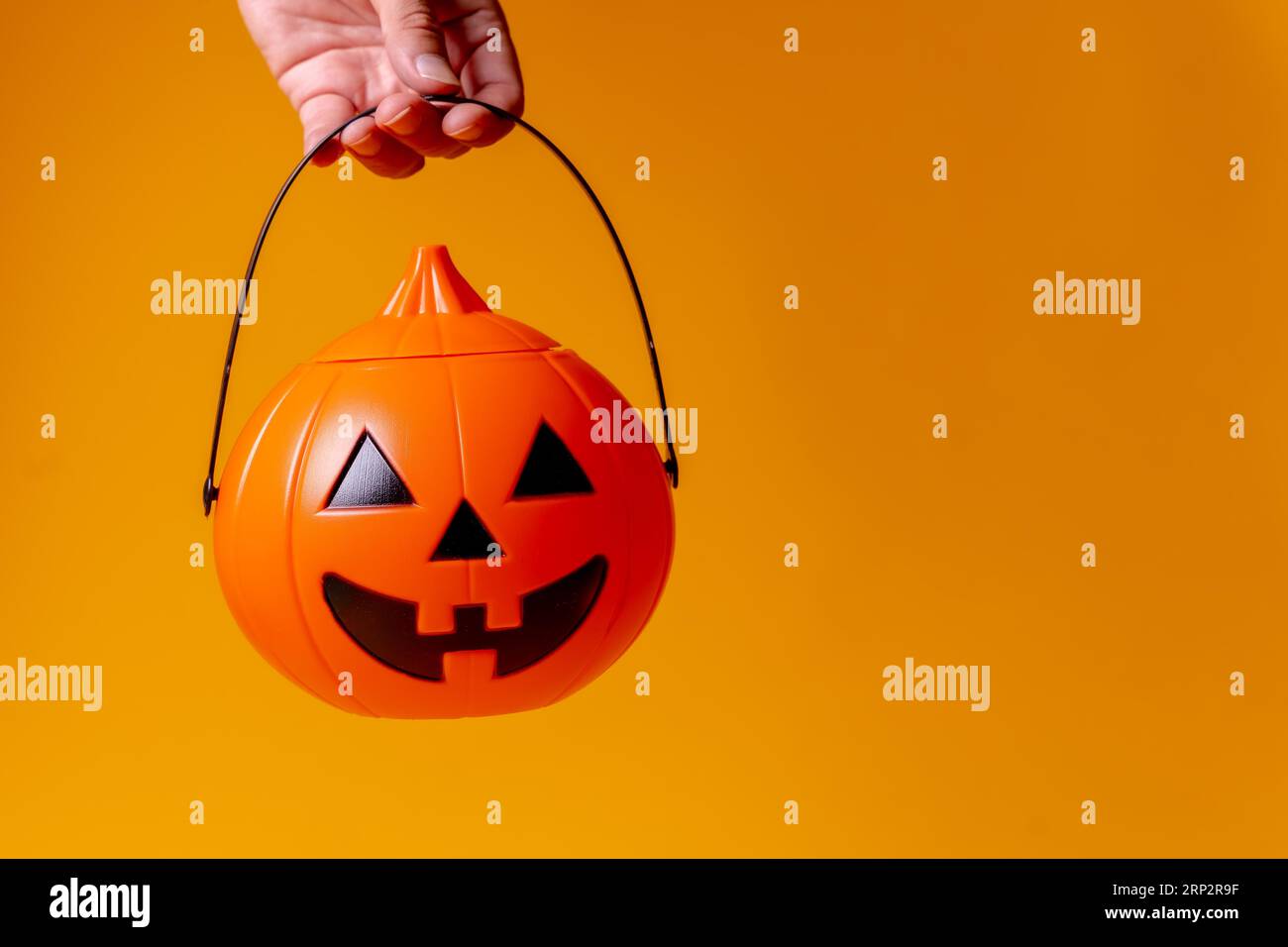 Hand hält einen orangefarbenen Halloween-Kürbis auf einem gelben Hintergrund Stockfoto