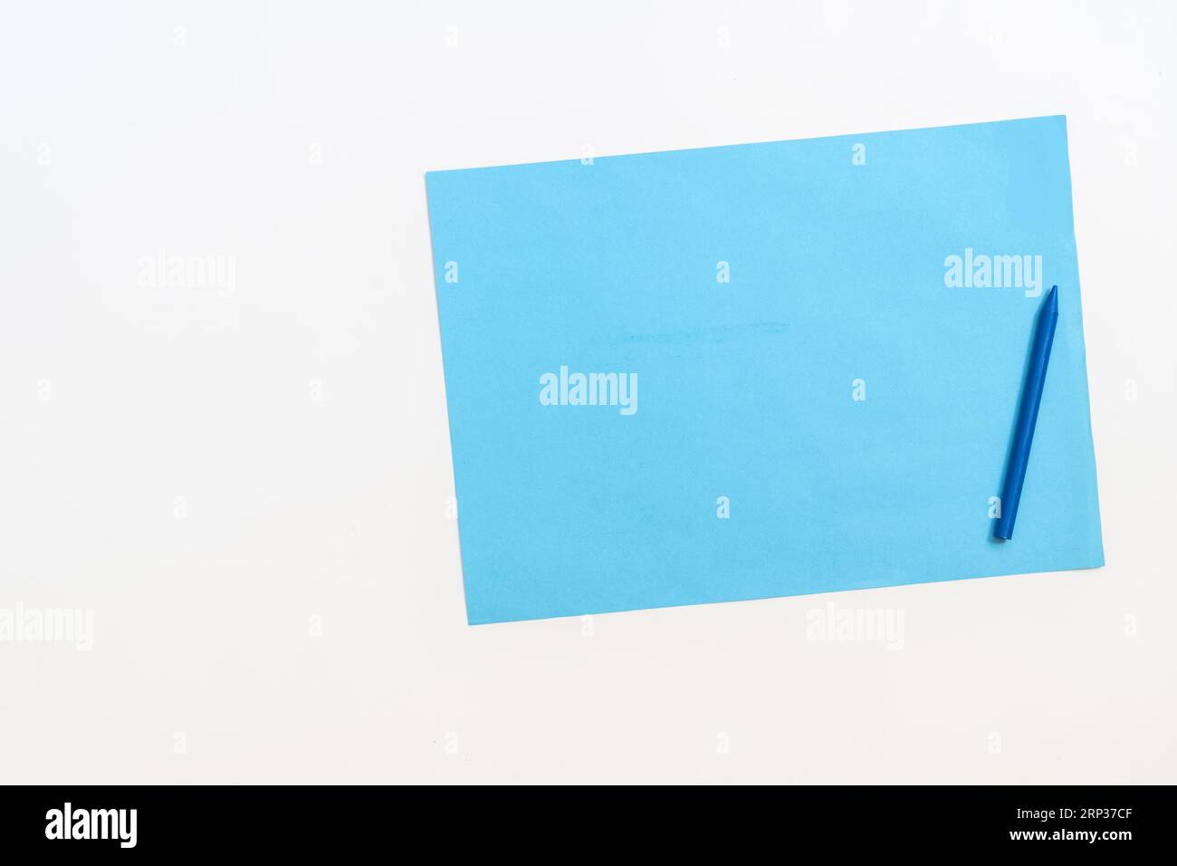Ein Blatt blaues Papier neben einem blauen Buntstift auf einer glatten weißen Oberfläche Stockfoto