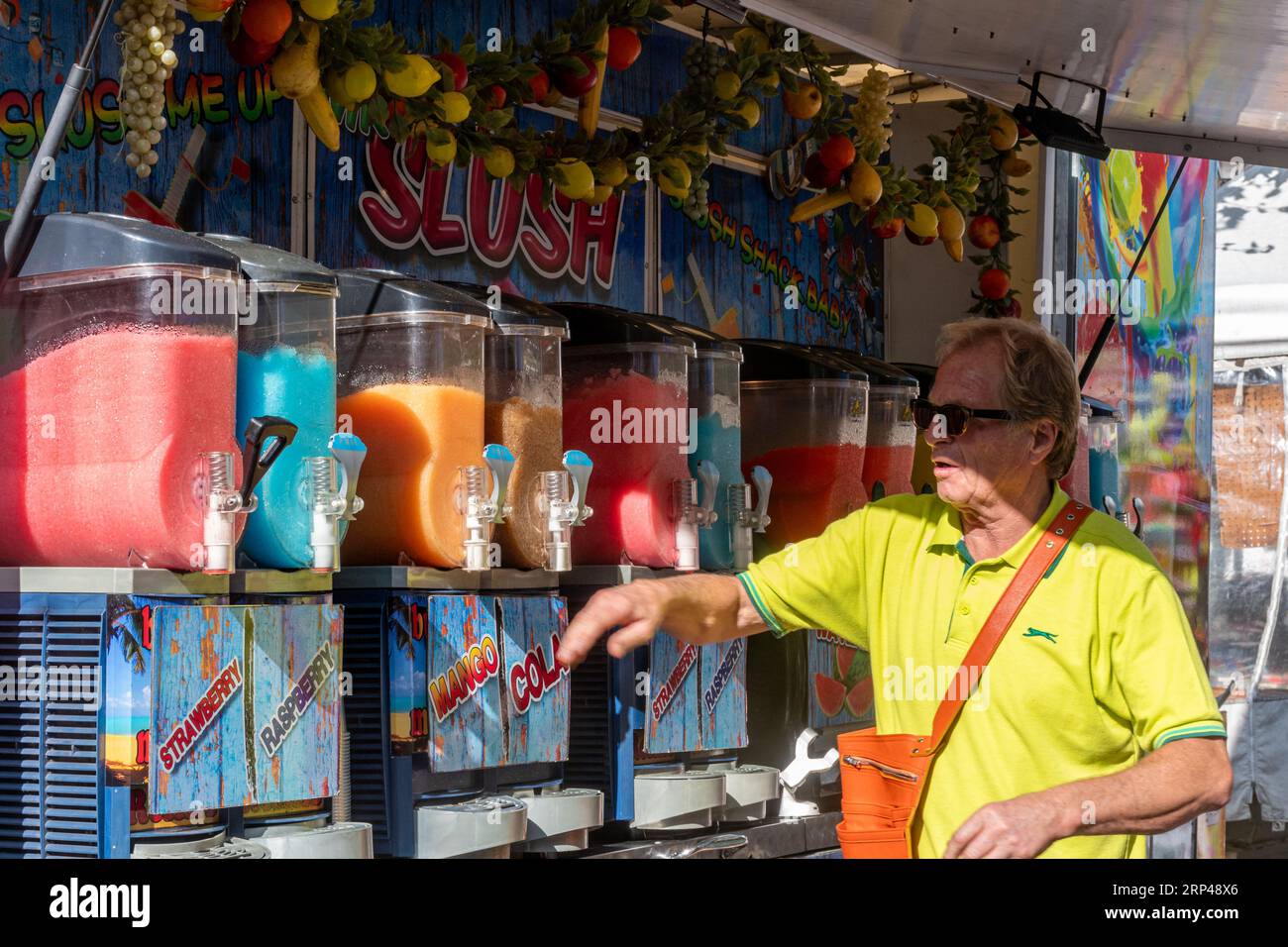 Slush Stand mit Mann, der bunte eiskalte Slushy Fruit Drinks auf einem Markt in Surrey, England, Großbritannien verkauft Stockfoto