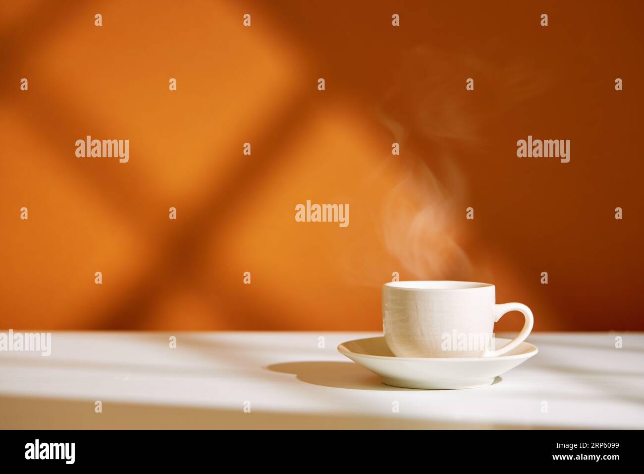 Nahaufnahme der Kaffeetasse auf dem Tisch bei direkter Sonneneinstrahlung. Morgenkaffee mit Dampf in weißer Tasse. Stockfoto