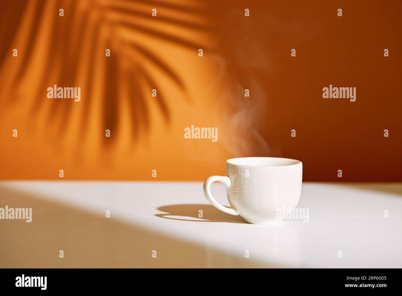 Nahaufnahme der Kaffeetasse auf dem Tisch bei direkter Sonneneinstrahlung. Morgenkaffee mit Dampf in weißer Tasse. Stockfoto