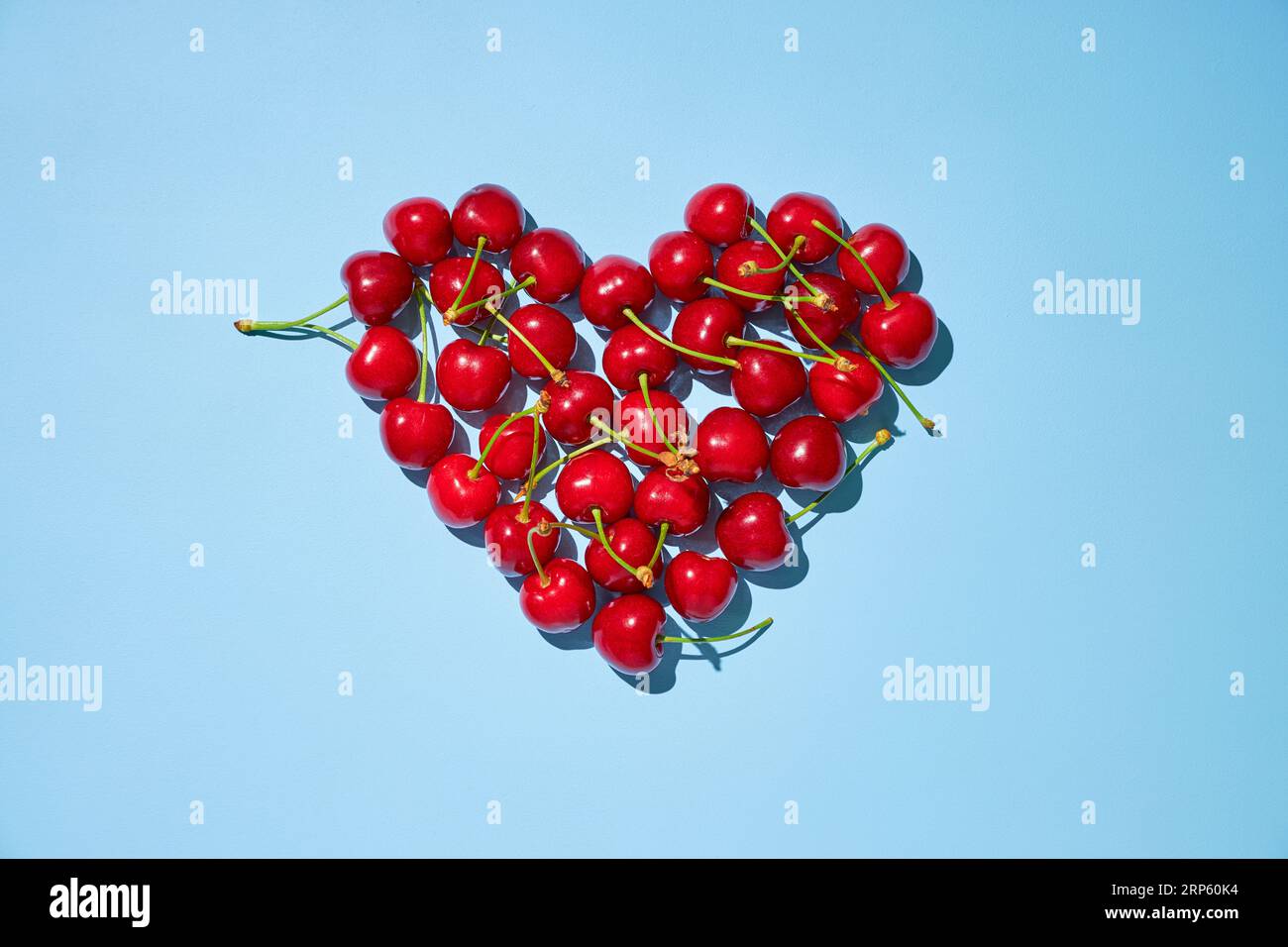 Frische reife rote Kirschen in Herzform auf blauem Hintergrund. Flach liegend. Stockfoto