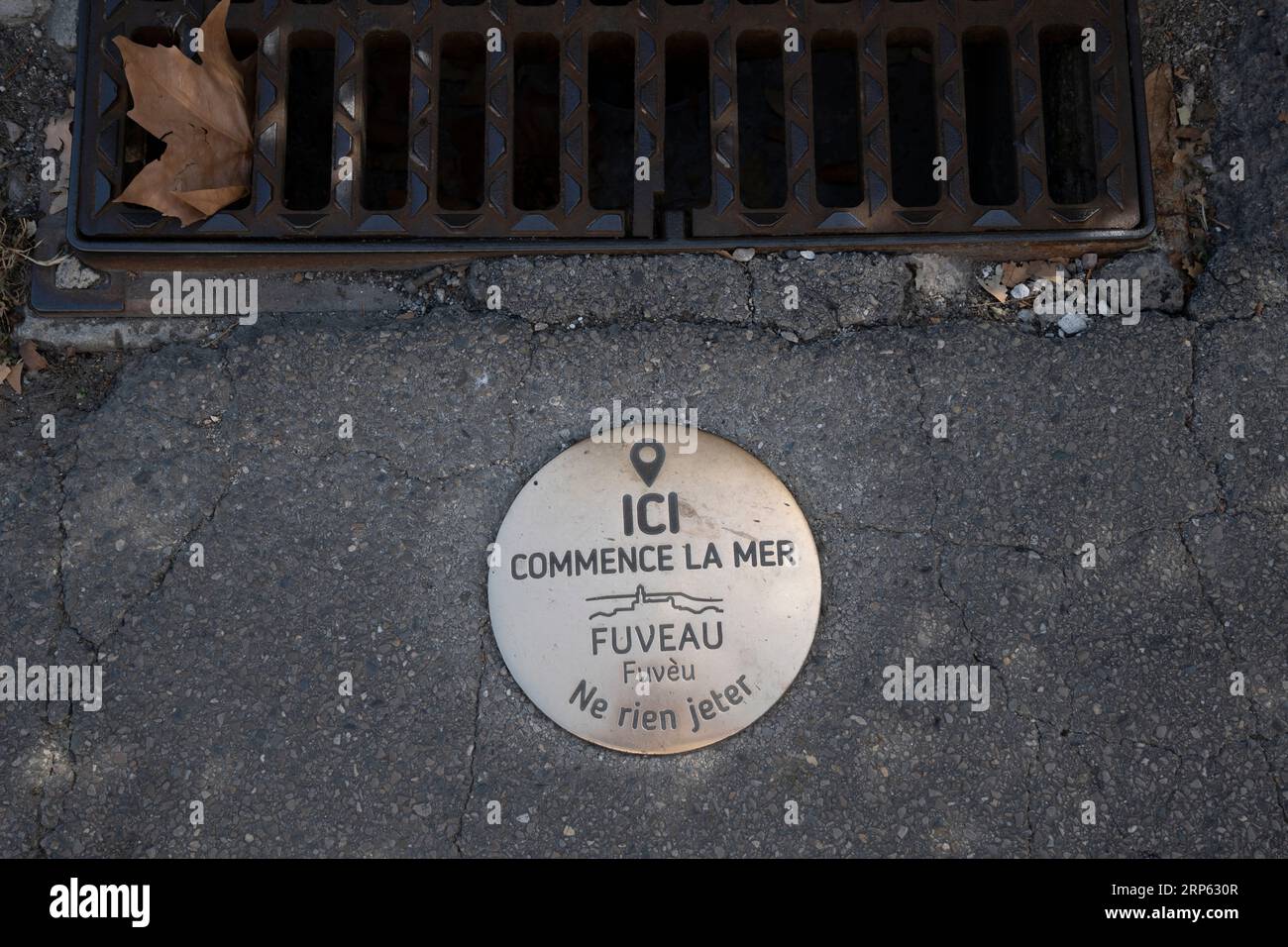 Bronzemagnagel-Kampagne gegen die Wasserverschmutzung mit der französischen Aufschrift „Here Begins the Sea, Fuveau, Don't Litter“. Fuveau, Frankreich Stockfoto