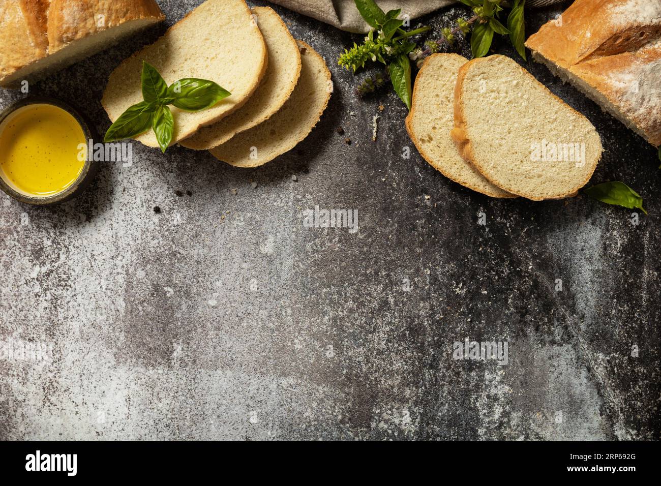 Geschnittenes italienisches Ciabatta-Brot mit extra nativem Olivenöl und Kraut auf dunklem Steinhintergrund. Frisches knuspriges Ciabatta-Brot. Ansicht von oben. Spac kopieren Stockfoto