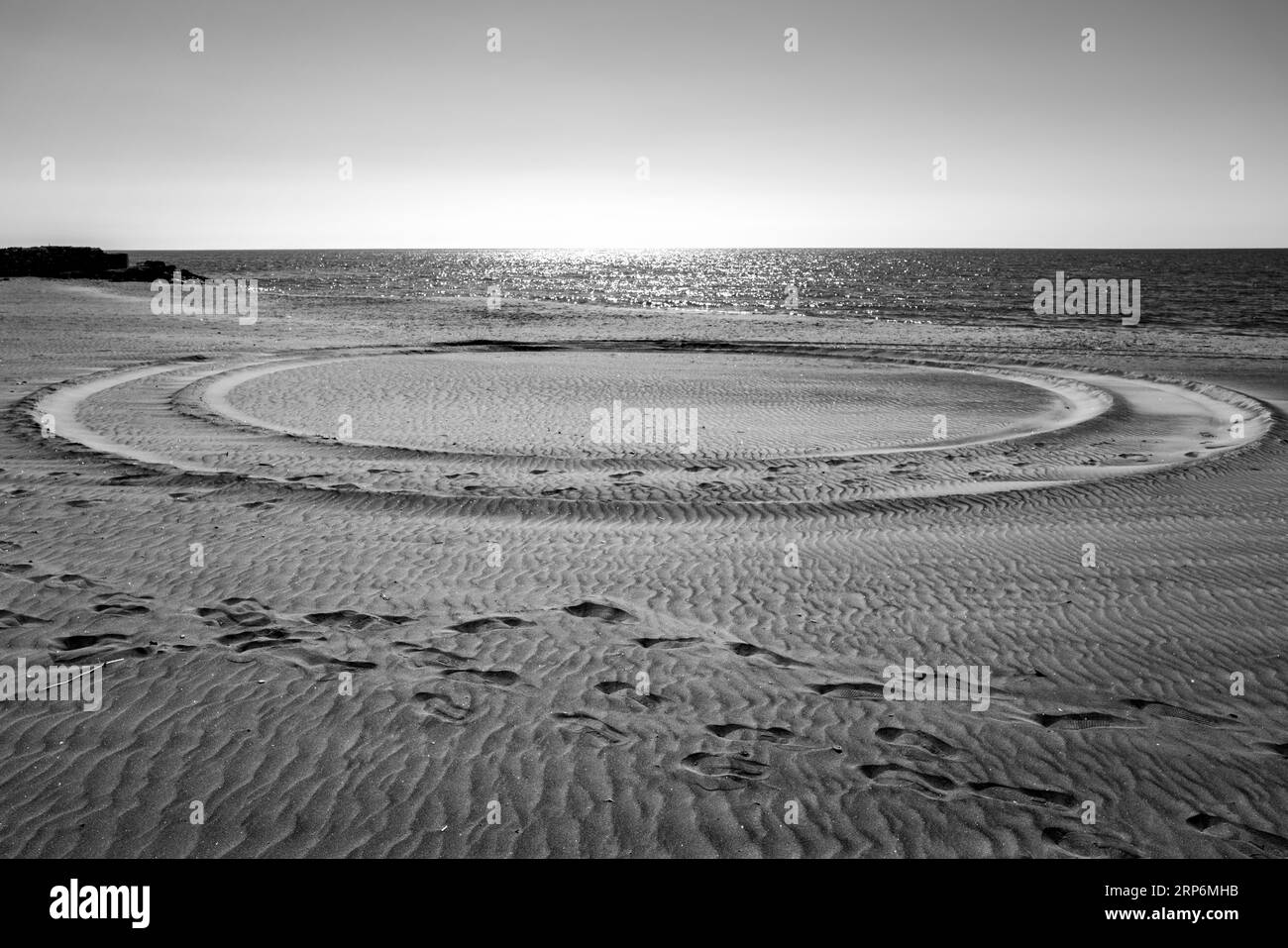 Meereslandschaft in Schwarz-weiß, mit einem Kreis aus Sand, der von Fußspuren durchzogen wird: Metaphysische Landschaft, Landschaften der Seele. Stockfoto
