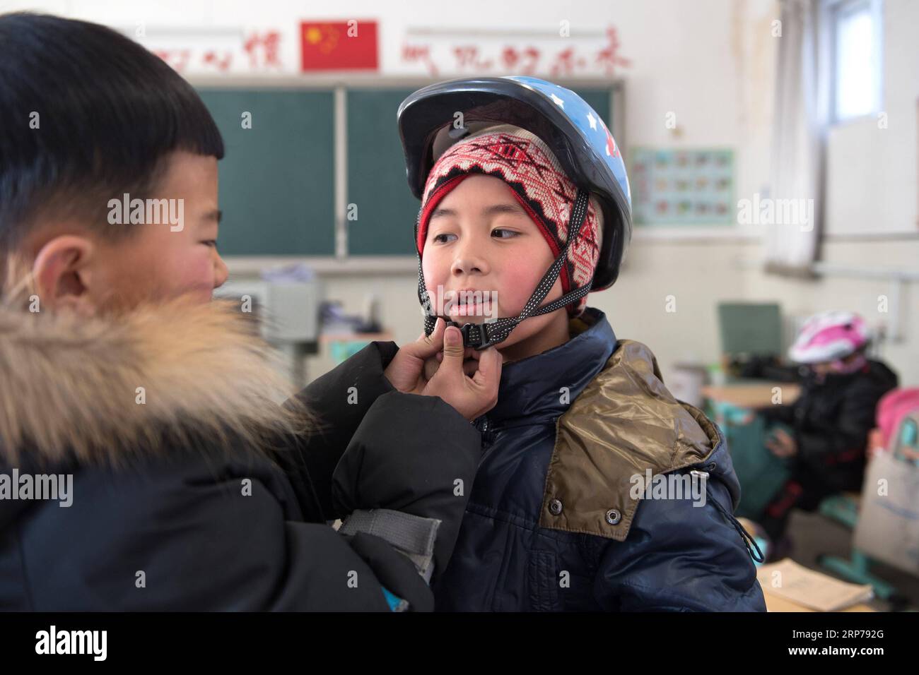 (190201) - Peking, Februar 1, 2019 (Xinhua) - Foto auf Jan. 10, 2019 zeigt einen Jungen helfen Cao Ming mit seinem Helm vor einem Training bei Taipingzhuang zentrale Grundschule im Landkreis Yanqing von Peking, der Hauptstadt von China. Taipingzhuang zentrale Grundschule direkt am Fuße des Xiaohaituo Bergen, wo die Veranstaltungsorte für Beijing 2022 Olympischen Winterspiele im Bau befinden. Die Lehrer der Taipingzhuang zentrale Grundschule haben eine experimentelle Ackerland in eine saisonale Eisbahn für die Schüler hier lernen, Skaten seit 2016 gedreht. Die Schule stellte eine Erfahrung Stockfoto