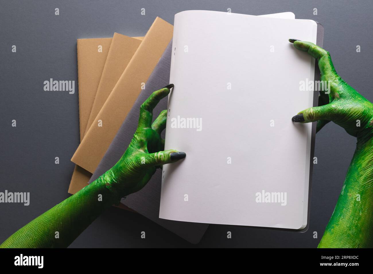 Grüne Monsterhände mit Notizbuch mit Platz für Kopien auf grauem Hintergrund Stockfoto