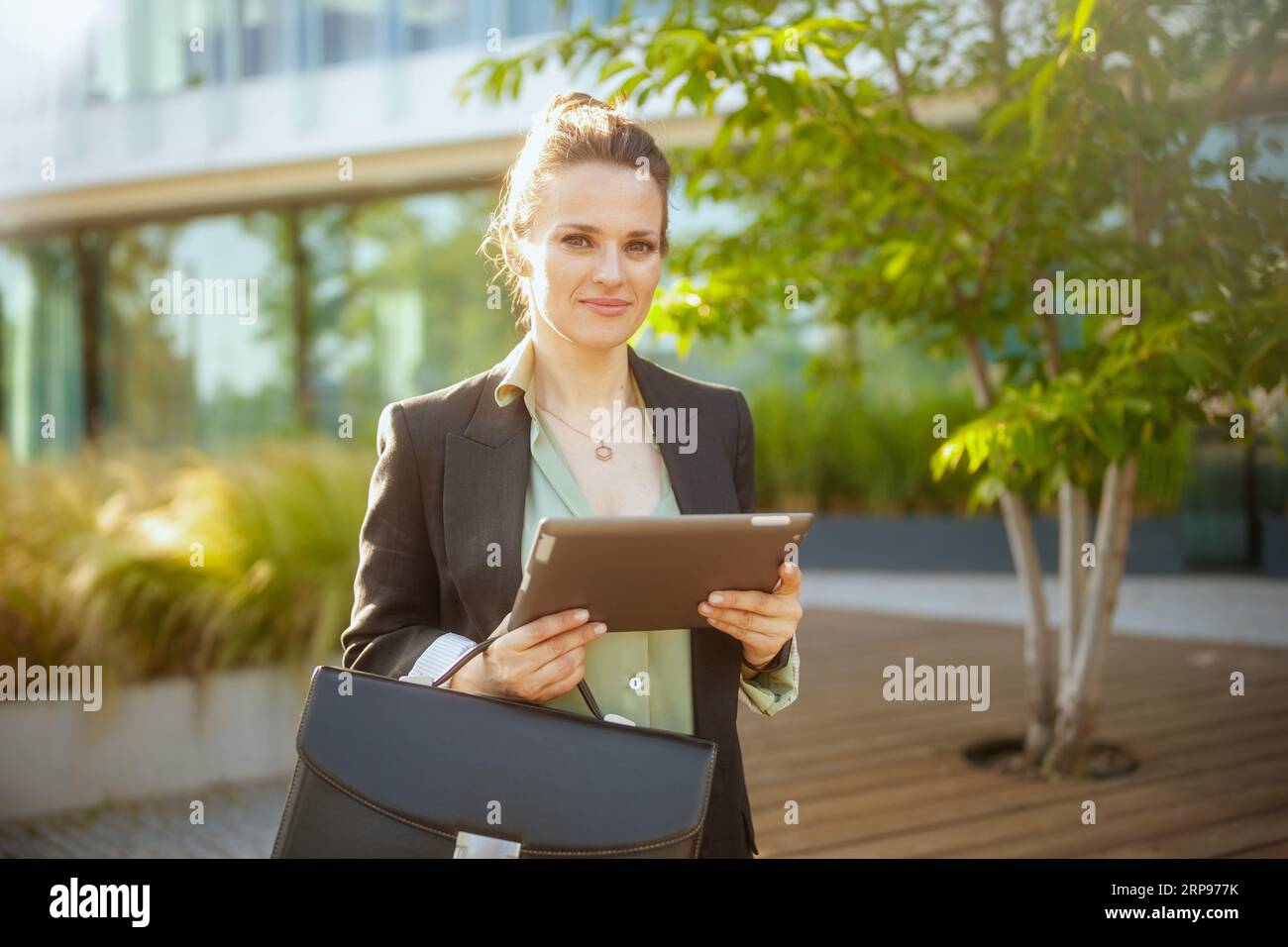 Moderne Arbeiterin im Geschäftsviertel in schwarzer Jacke mit Aktentasche mit Tablet-PC. Stockfoto