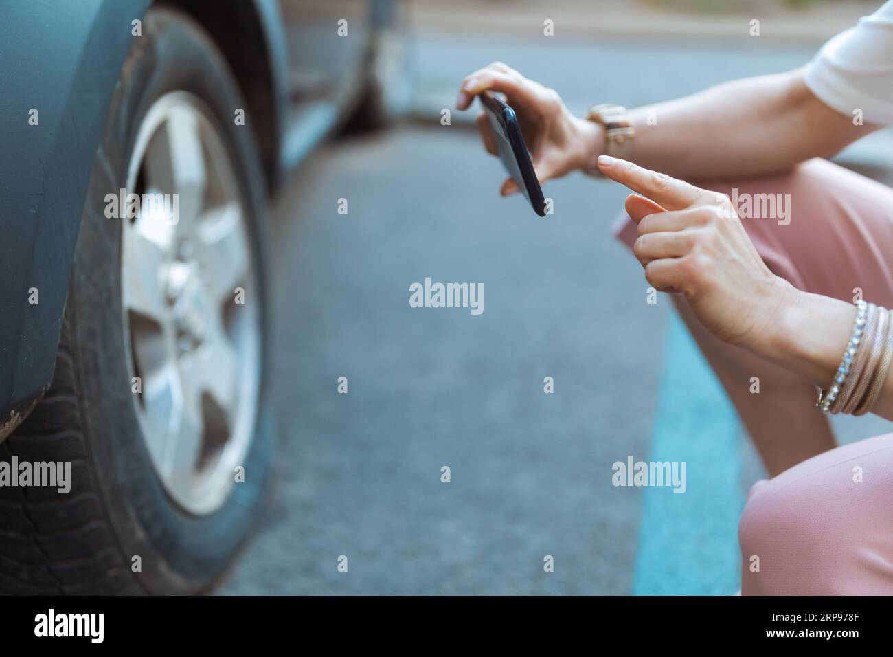 Autounfall. Nahaufnahme einer Reisenden Frau in der Stadt mit Smartphone, die ein Foto in der Nähe eines Autos mit einem Platten Reifen macht. Stockfoto