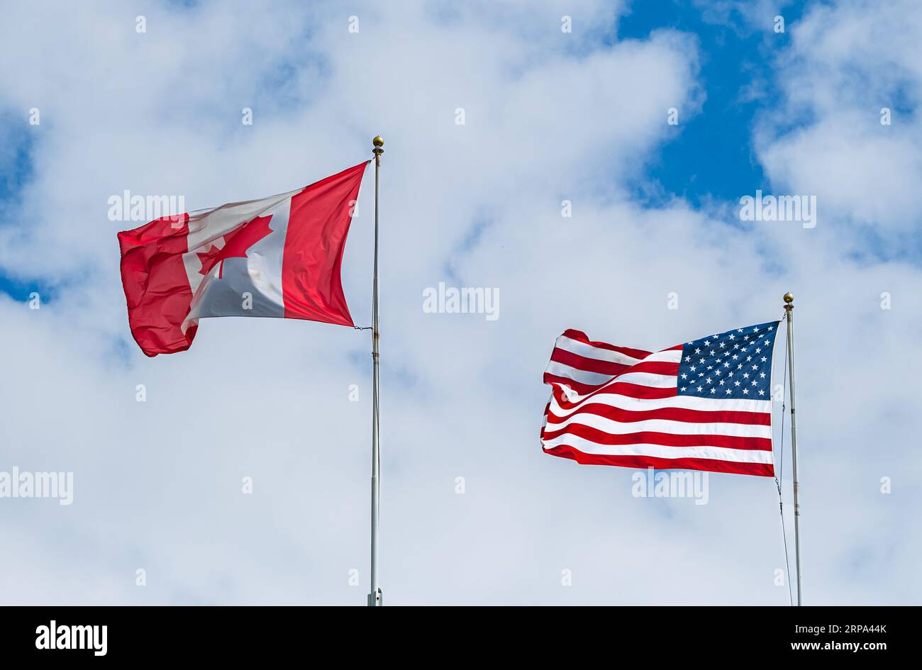 Flagge von Kanada und den USA vor dem Hintergrund des blauen Himmels mit weißen Wolken. Die amerikanische und kanadische Nationalflagge weht mit Stoffgewebe am Himmel. Stockfoto