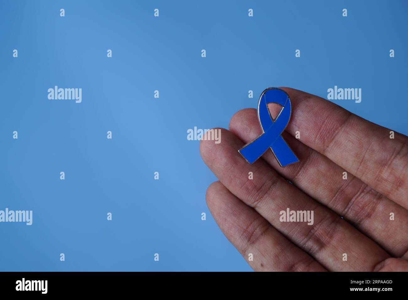 Hand hält blaues Band auf blauem Hintergrund mit Kopierraum. Krebsbewusstseinskonzept Stockfoto