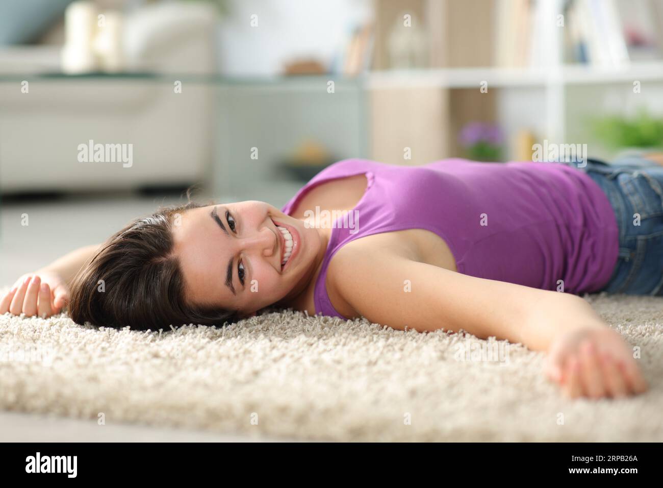 Glückliche Frau zu Hause, die die Kamera auf einem Teppich ansieht Stockfoto