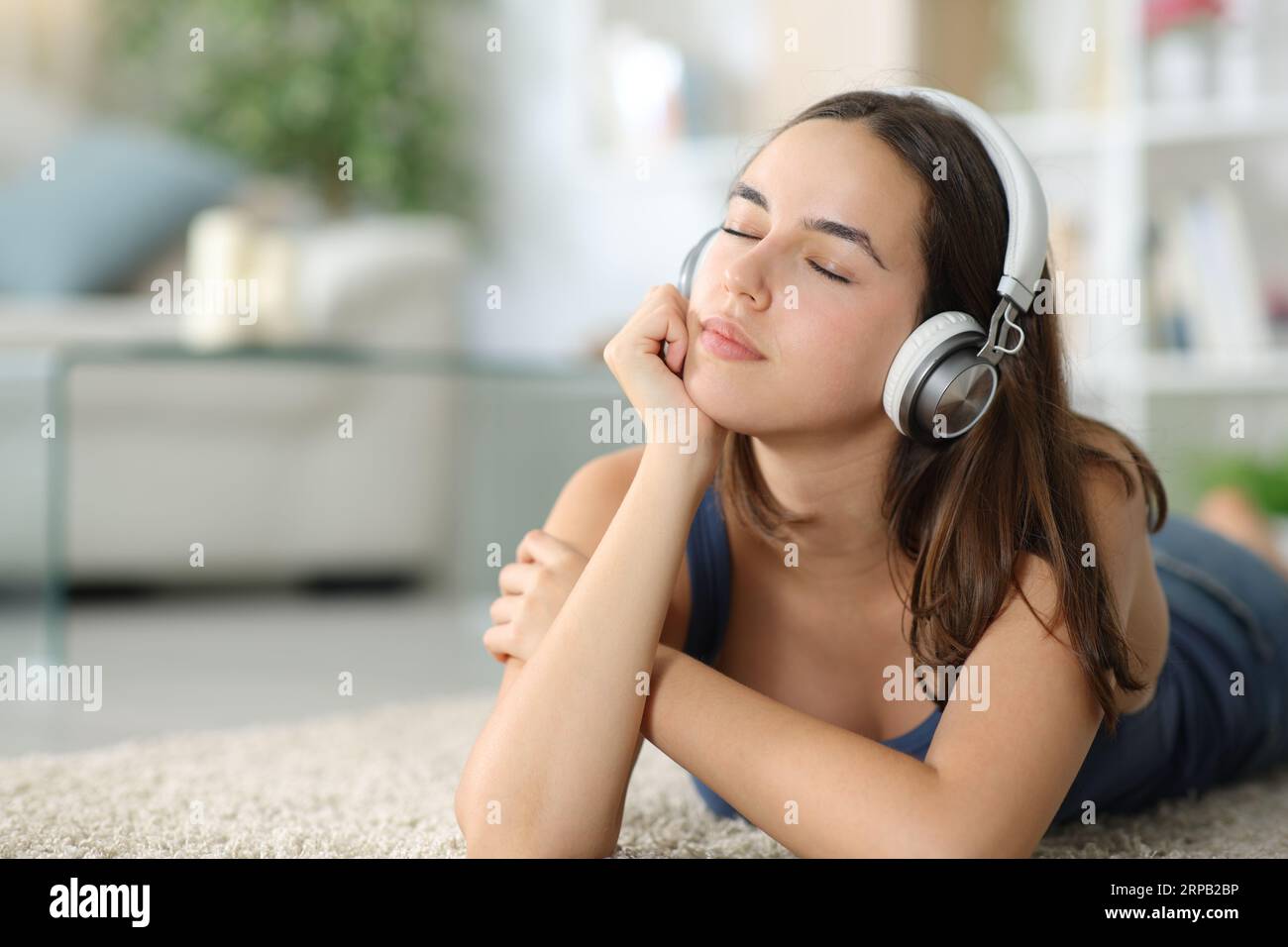 Entspannte Frau, die Musik hört, während der Kopfhörer zu Hause auf dem Boden liegt Stockfoto