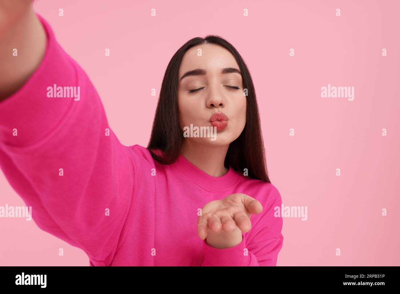 Junge Frau, die Selfie macht und Küsschen auf rosa Hintergrund bläst Stockfoto