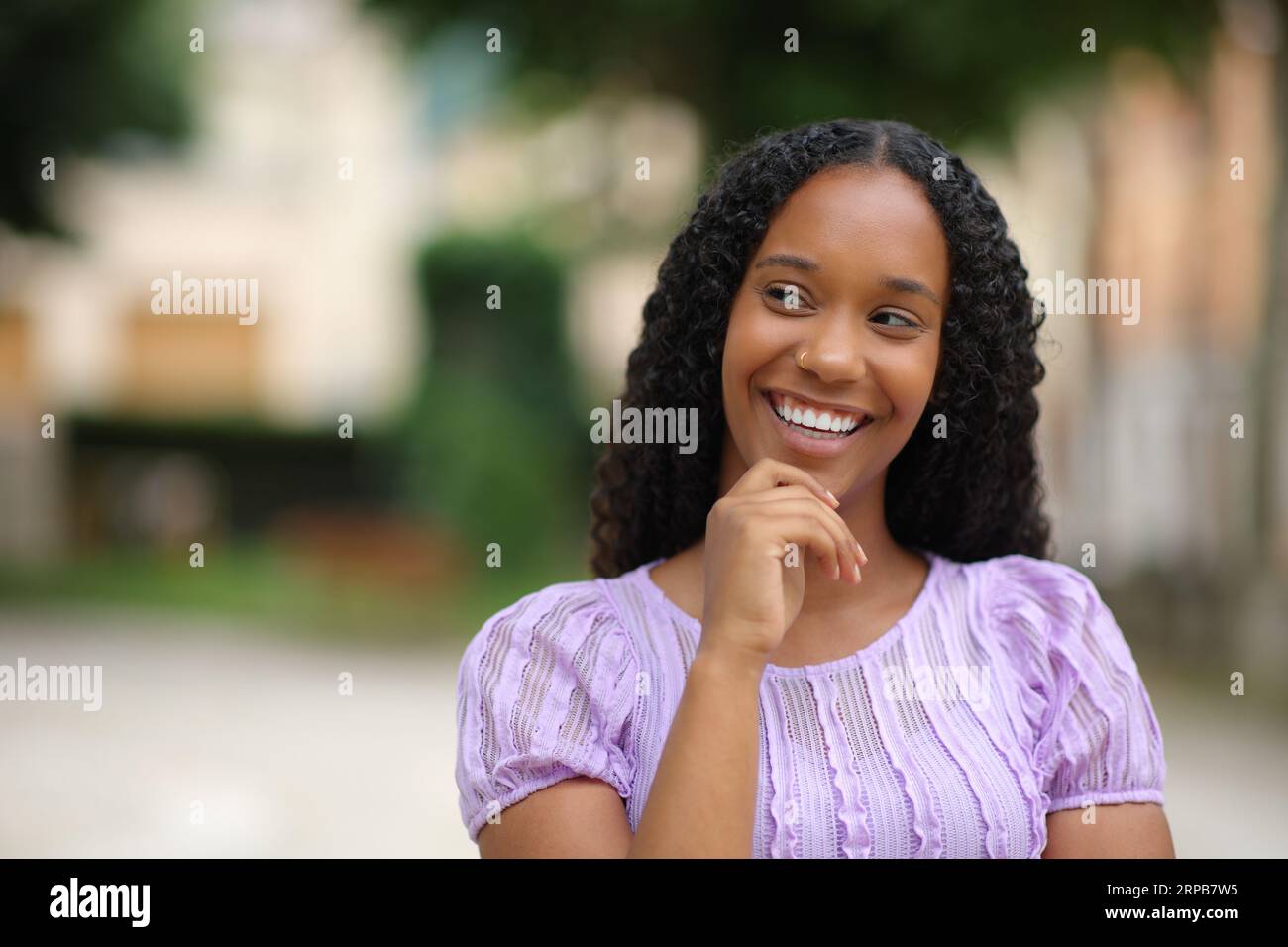 Vorderansicht eines Porträts einer glücklichen schwarzen Frau, die an der Seite auf der Straße denkt Stockfoto
