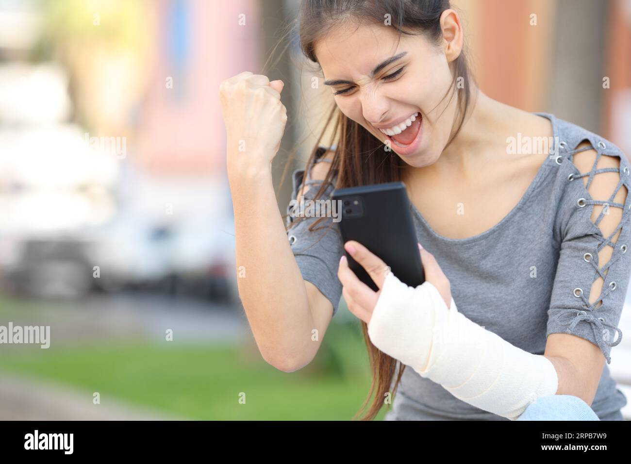 Aufgeregte Rekonvaleszenzfrau feiert gute Nachrichten und überprüft das Telefon auf der Straße Stockfoto