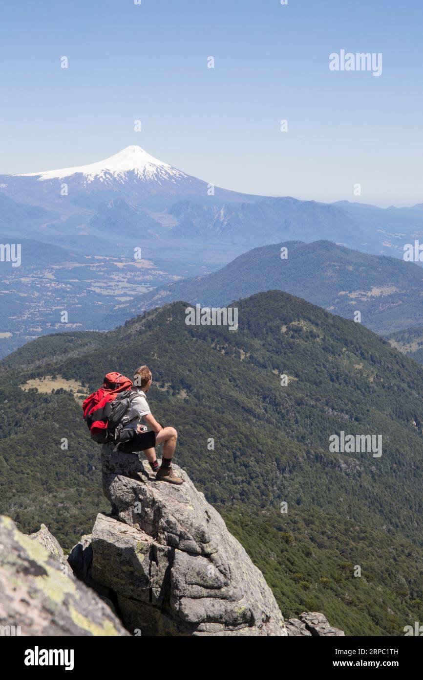 Der Wanderer sitzt auf einem Felsvorsprung mit einem Vulkan in der Ferne Stockfoto