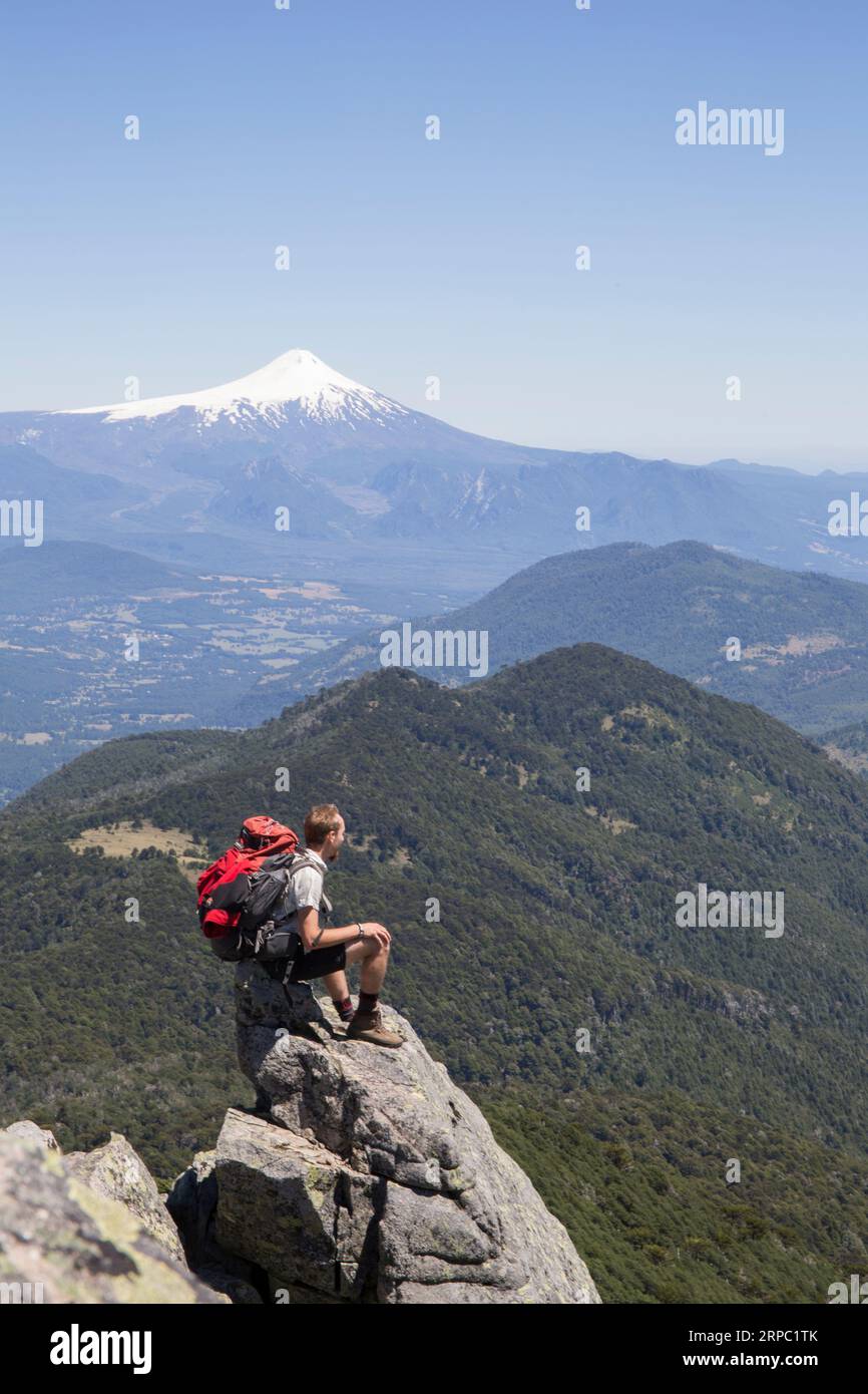 Der Wanderer sitzt auf einem Felsvorsprung mit einem Vulkan in der Ferne Stockfoto