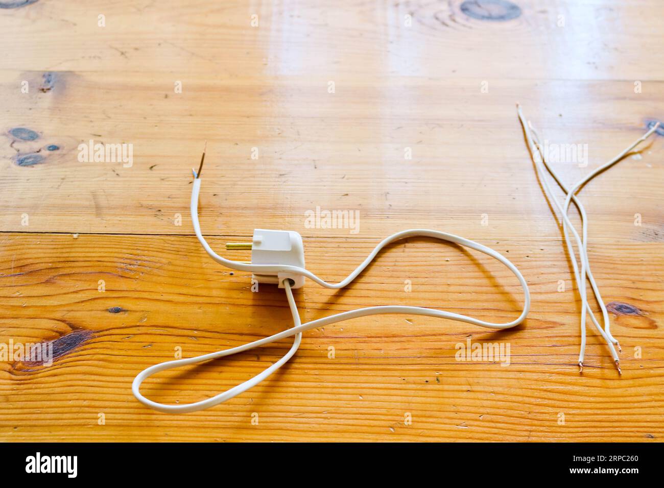 Weiße freistehende elektrische Drähte mit einem elektrischen Stecker für eine Steckdose auf einem Holztisch. Stockfoto