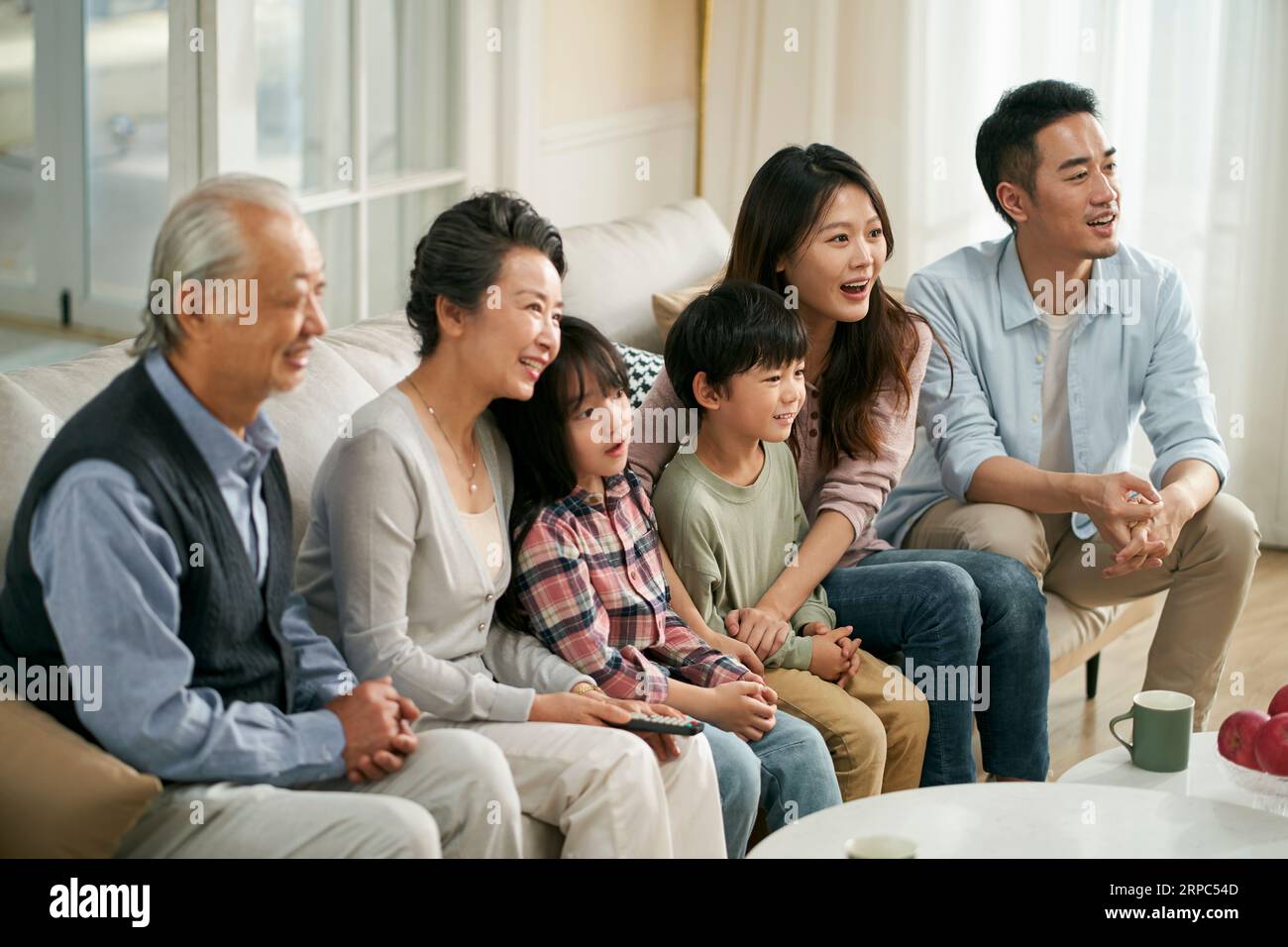 Eine asiatische Familie der 3. Generation, die zu Hause auf der Couch sitzt und zusammen fernsieht, glücklich und lächelnd Stockfoto