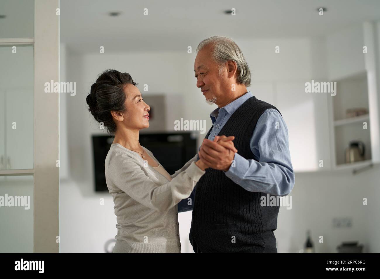 Liebevoll romantisches asiatisches Seniorenpaar, das zu Hause im Wohnzimmer tanzt Stockfoto