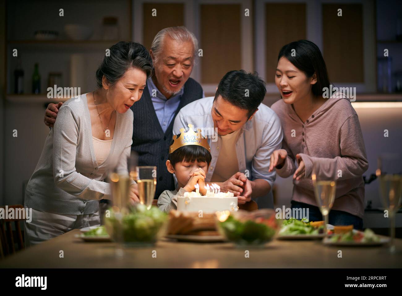 Ein kleiner asiatischer Junge, der sich wünscht, während die Familie in drei Generationen zu Hause seinen Geburtstag feiert Stockfoto