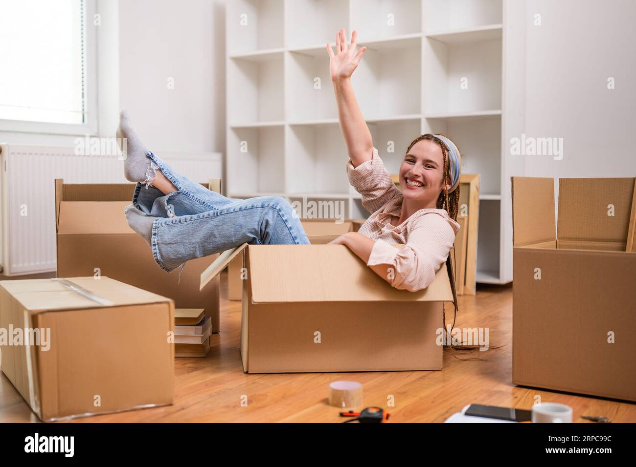 Glückliche Frau winkt, während sie in der Box sitzt und Spaß in ihrem neuen Zuhause hat. Stockfoto