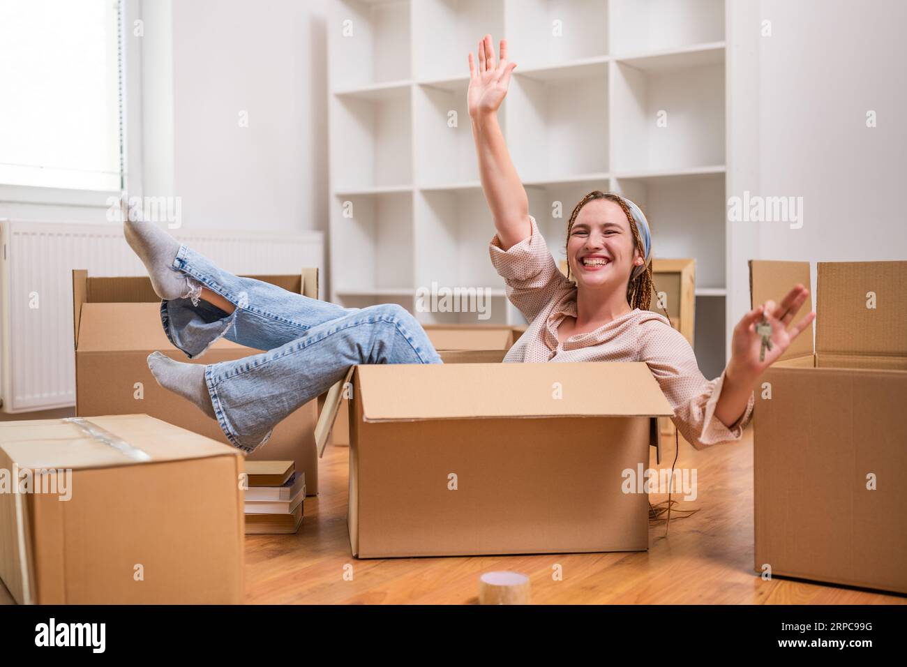 Glückliche Frau, die den Schlüssel ihres neuen Zuhauses zeigt, während sie in der Box sitzt und Spaß hat. Stockfoto