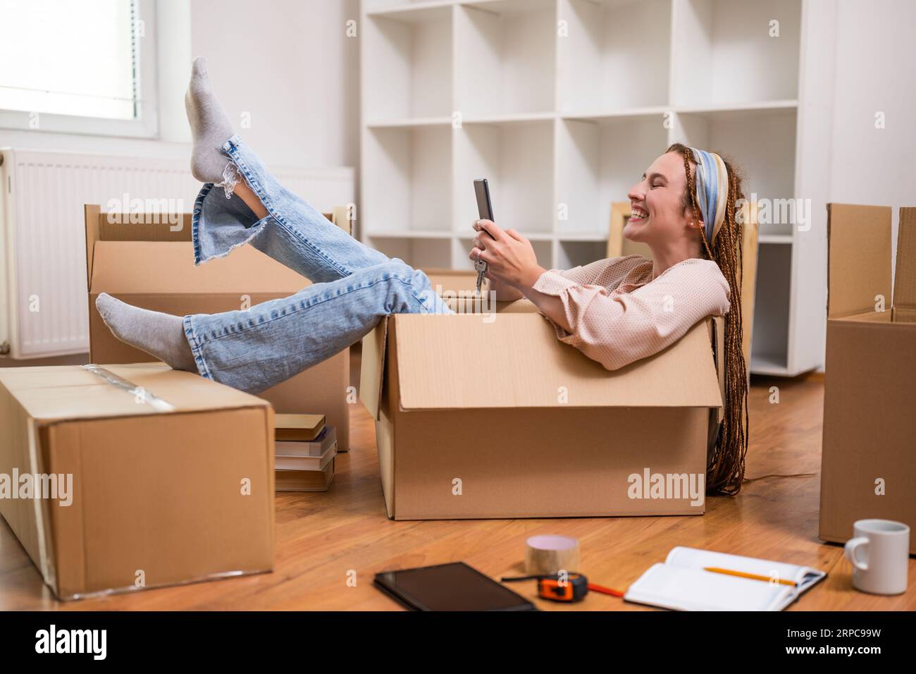 Glückliche Frau, die ein Telefon benutzt und Spaß hat, während sie in eine neue Wohnung zieht. Stockfoto