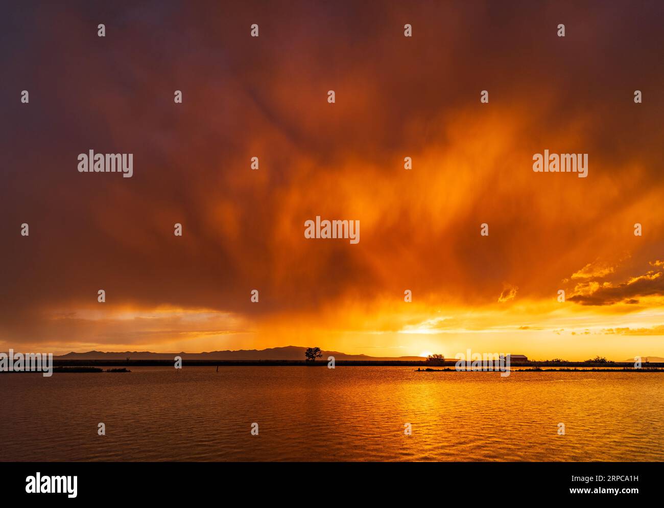 Ein feuriger Sonnenuntergang erhellt die Sturmwolken und reflektiert die Gewässer der Farmington Bay Waterfowl Management Area, Farmington, Davis County. Utah, USA Stockfoto