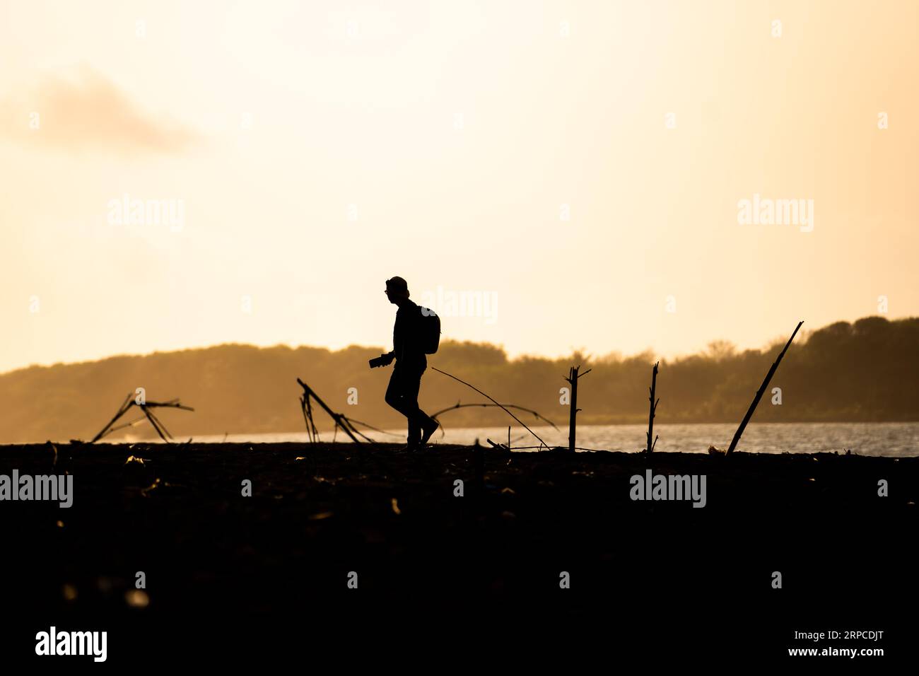 Silhouette eines Abenteurers, der an der Küste entlang spaziert und Fotos macht, Blick auf den Sonnenuntergang. Motivationskonzept. Stockfoto