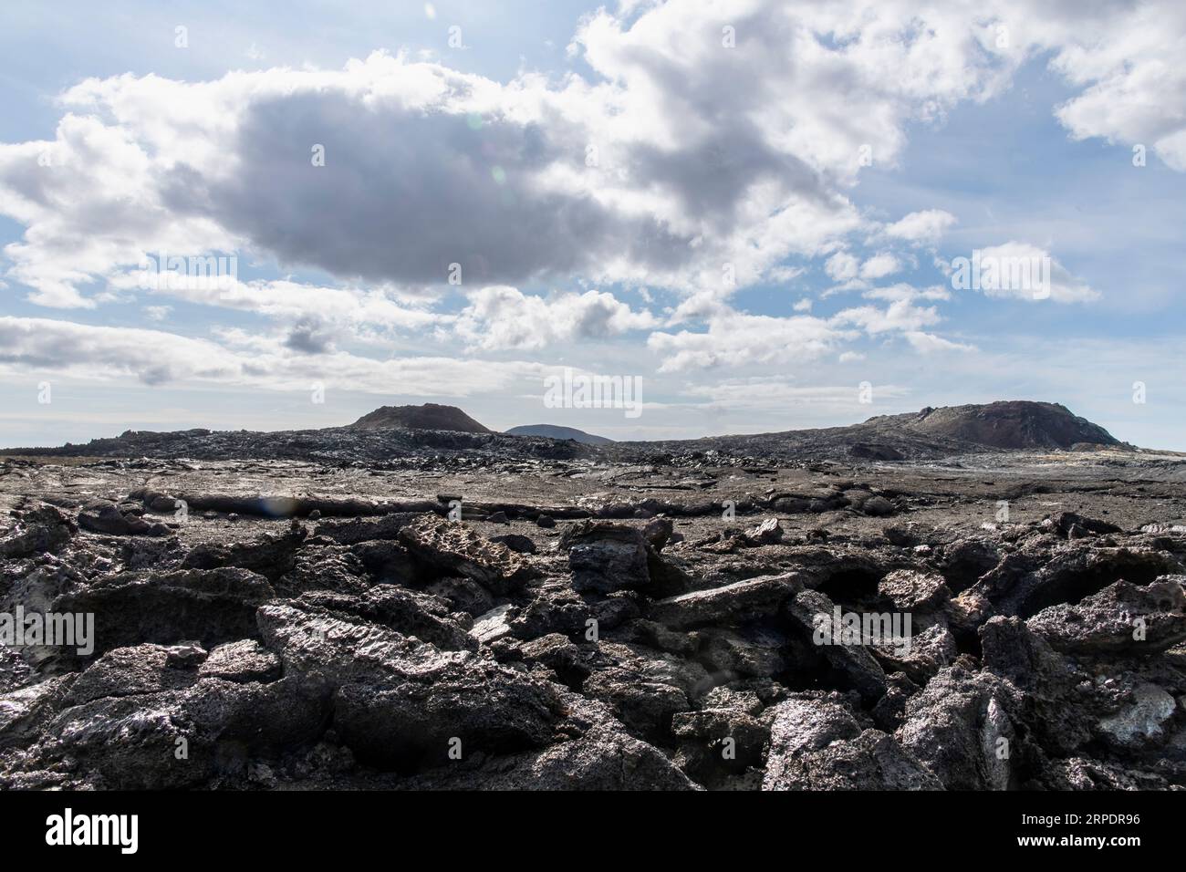 Blick aus niedrigem Winkel auf die gebrochene Lava im Lavafeld in der Nähe des Berges Fagradalsfjall mit Spalten von 2021 und 2022 im Gebiet des Geldingadalir-Vulkans bis zum Gipfel Stockfoto