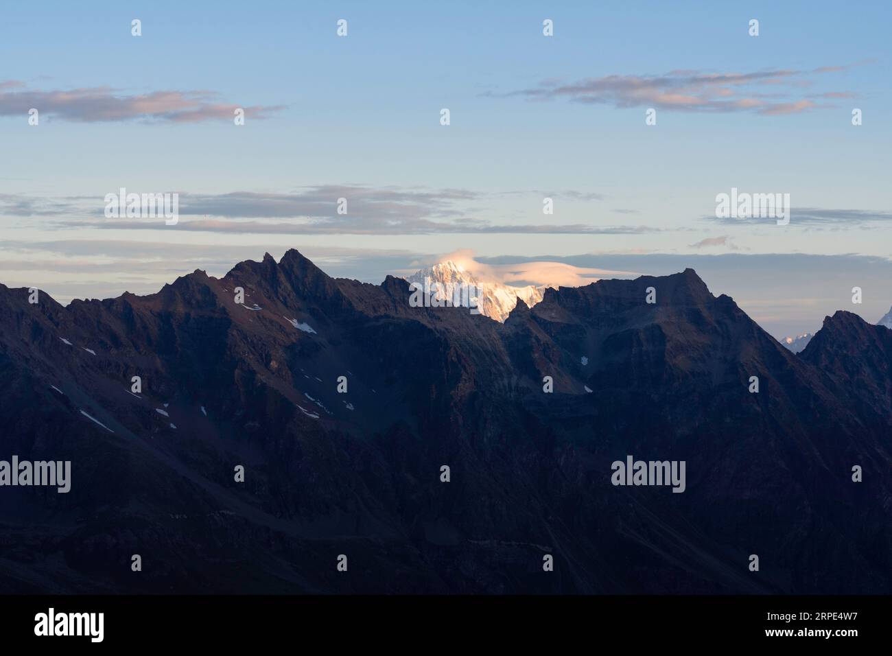 Blick auf den Mont Blanc vom Gletscher des Gran Paradiso Nationalparks bei Sonnenaufgang. Orange gelbe Spitze im Hintergrund, Berge und Tal im Schatten Stockfoto