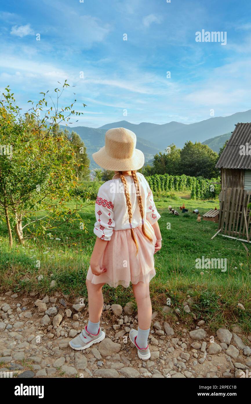 Ukrainisches Kind mit langen geflochtenen Haaren in authentischem Kostüm auf dem Bauernhof in den Karpaten Dorf niedliches Mädchen gesticktes Hemd landschaftlich reizvolle Aussicht. Unabhängig Stockfoto