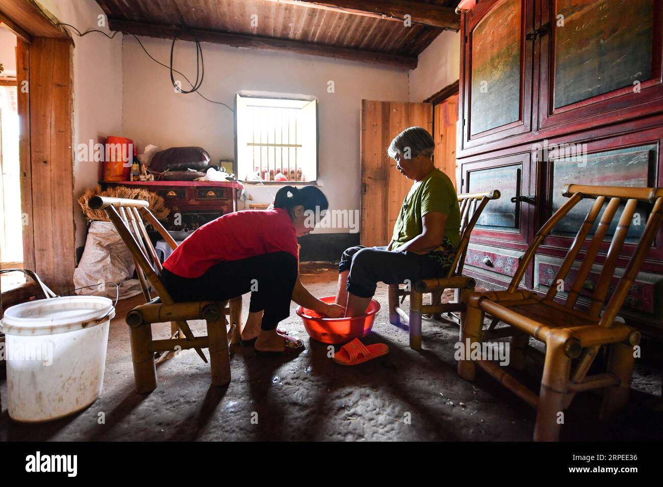 (190826) -- NANCHANG, 26. August 2019 -- Liu Lihong (L) hilft ihrer Schwiegermutter, die Füße zu Hause in der Dabaidi Township der Stadt Ruijin in der ostchinesischen Provinz Jiangxi zu baden, 19. August 2019. Liu Lihong trägt eine schwarze Baskenmütze und ein Paar High-Heels und frittiert Fleisch und Gemüse in Kochherden, während sie Musik hört, eine typische Szene in ihrer täglichen Routine. Der 40-jährige Koch arbeitet seit drei Jahren für die lokale Regierung der Gemeinde Dabaidi. Bevor er professioneller Koch wurde, war Liu seit dem als Wanderarbeiter in einer Bekleidungsfabrik in Shantou in der südchinesischen Provinz Guangdong tätig Stockfoto